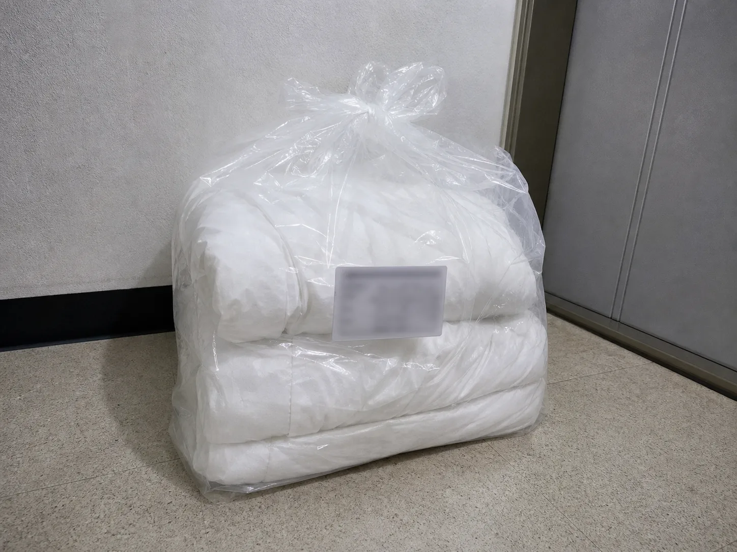 현관 앞 투명 비닐 봉투 안에 접힌 흰 이불 커버