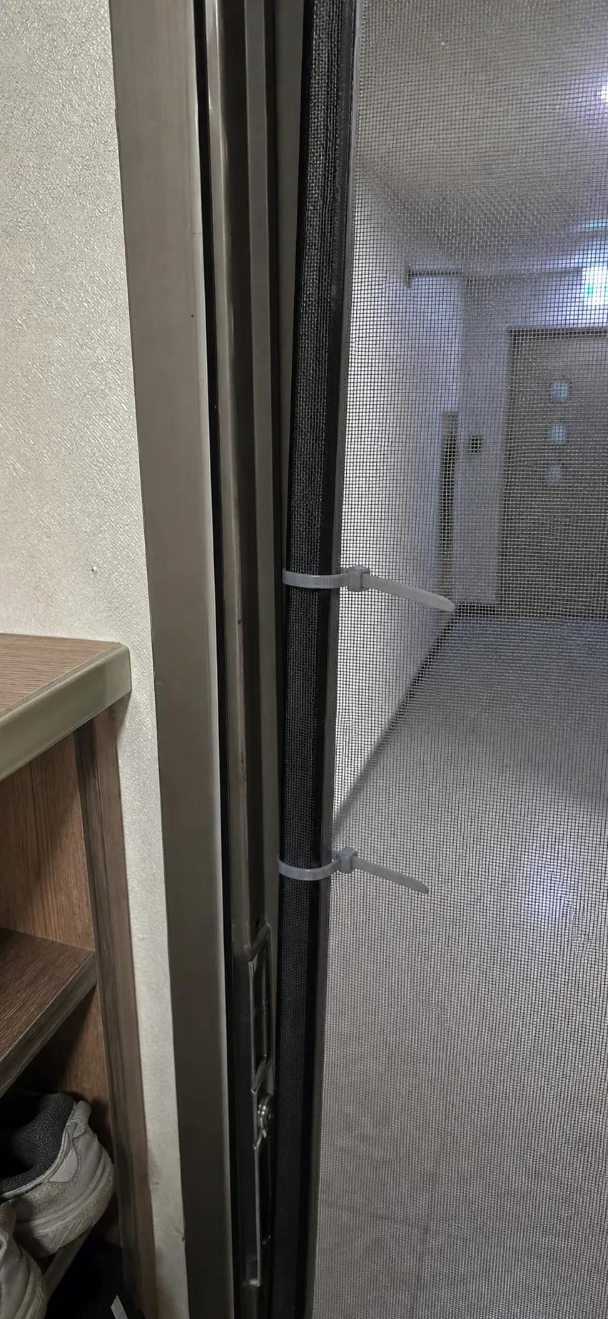 현관 방충망 안쪽에 회색 케이블타이 두 개가 묶인 모습